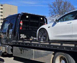 A black flatbed tow truck from Pro-Tech Wrecker Service towing a white Tesla in Decatur, AL.