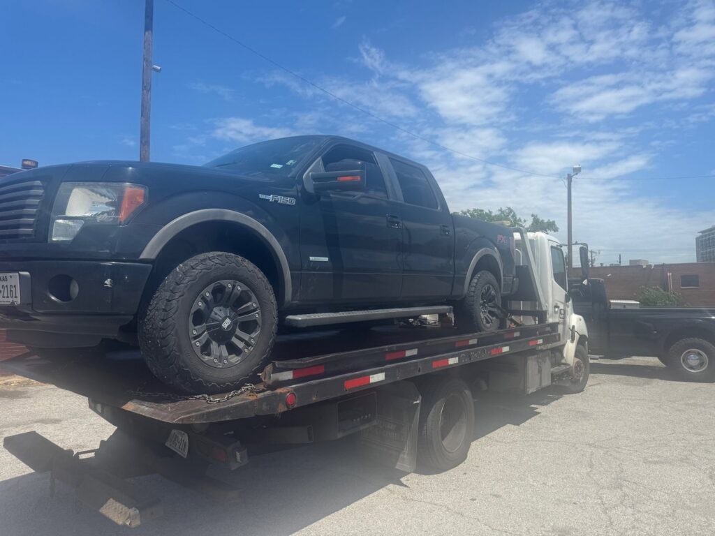 A black Ford F-150 pickup truck being transported on a flatbed tow truck by Towing Near Me 247 LLC in Irving, TX.