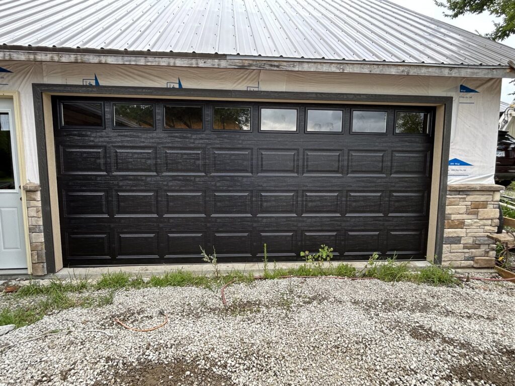 A modern black garage door with windows installed on a new construction home by Woodwards Overhead Door Co. in Topeka, KS