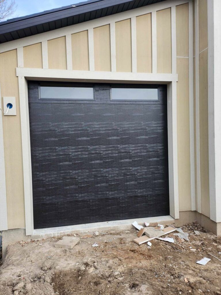 A black garage door with two top windows on a new construction site by Layton Doors in West Jordan, UT.
