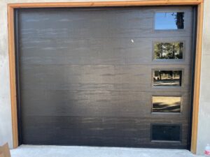 A modern black garage door with several small windows, installed by Quality-Brand Garage Doors in Rio Rancho, NM.