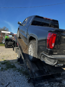 A black GMC Sierra pickup truck being loaded onto a flatbed tow truck by Heavy Hookz Towing in Fort Worth, TX.