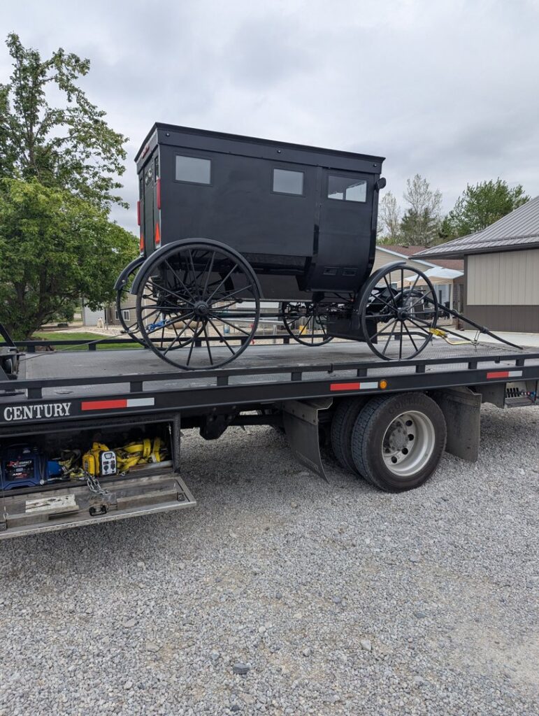 A black horse-drawn buggy being transported on a flatbed tow truck by First Hand Towing & Recovery in Fort Wayne, IN.