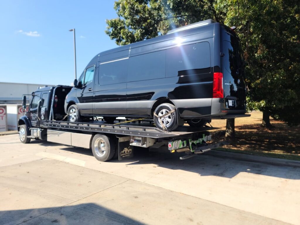 A black Mercedes Sprinter van being towed on a flatbed truck by Pro-Tech Wrecker Service in Decatur, AL.