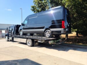 A black Mercedes Sprinter van being towed on a flatbed truck by Pro-Tech Wrecker Service in Decatur, AL.