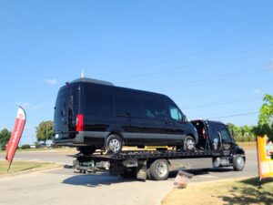 A black Mercedes Sprinter van being towed on a flatbed truck by Pro-Tech Wrecker Service in Decatur, AL.