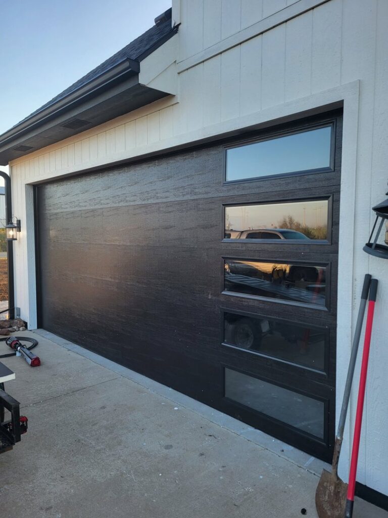 A black modern garage door with vertical windows installed on a new home by ABC Garage Doors KC in Kansas City, KS.