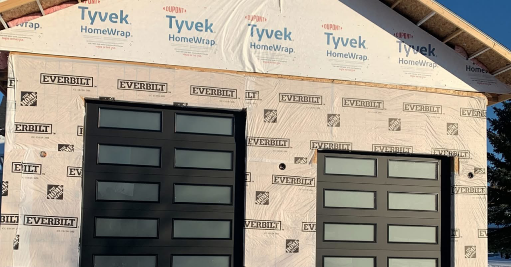 Black modern garage doors with multiple windows installed on a building under construction by Devildog Dock N Door in Helena, MT.