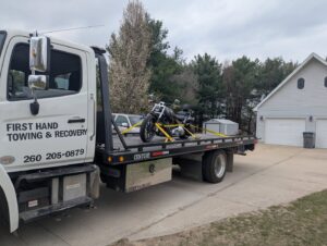 A black motorcycle being transported on a flatbed tow truck by First Hand Towing & Recovery in Fort Wayne, IN.