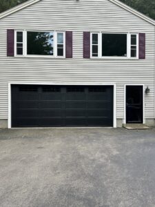A black panel garage door with multiple windows installed on a light-colored house by NDI Garage Door in Plaistow, NH.
