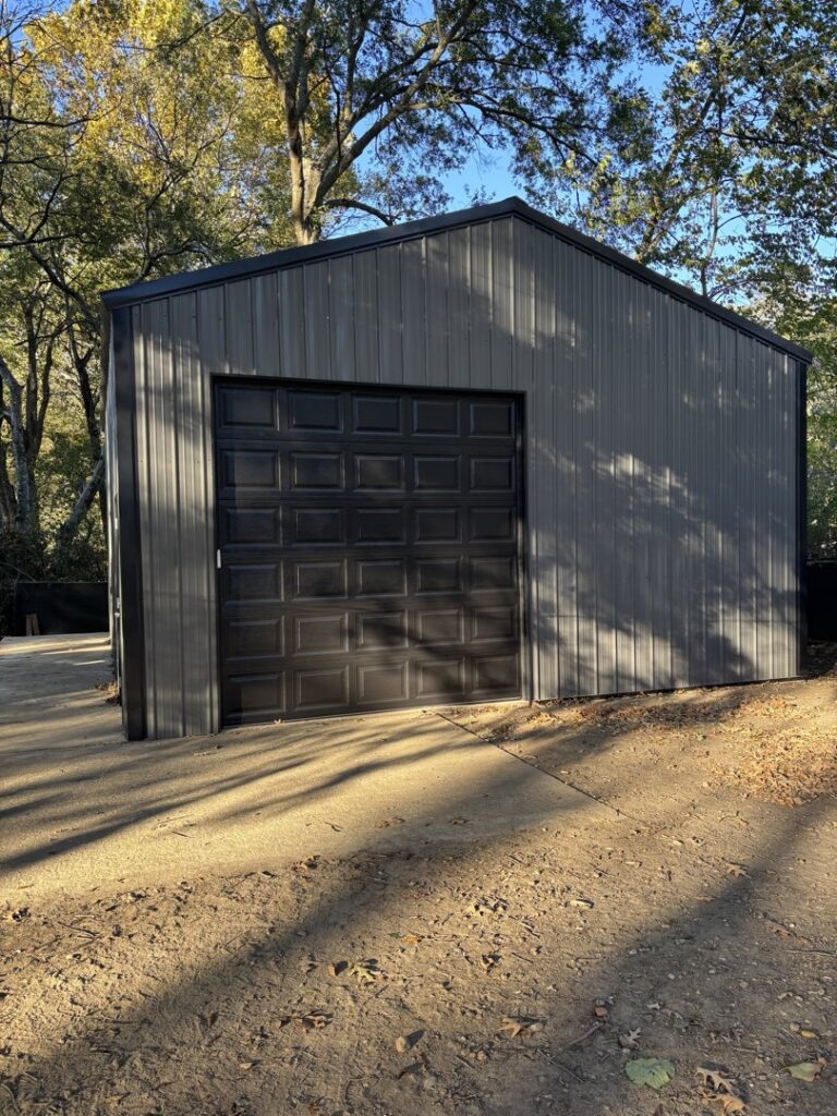 A black paneled garage door installed on a gray metal building by LaFrancis Overhead Door LLC in Little Rock, AR