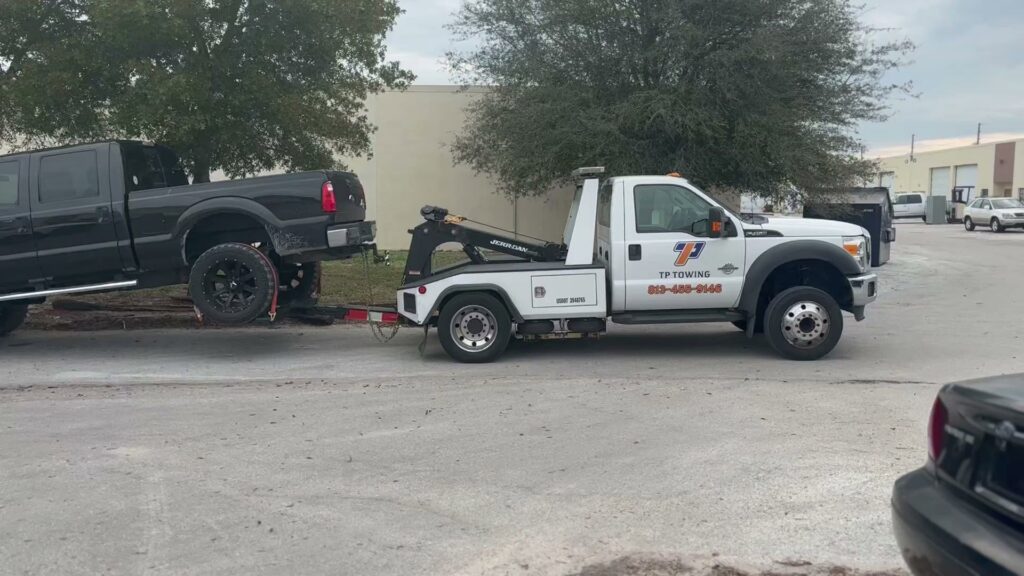 A black pickup truck being towed by a TP Towing wheel lift truck, providing heavy-duty towing in Tampa, FL.