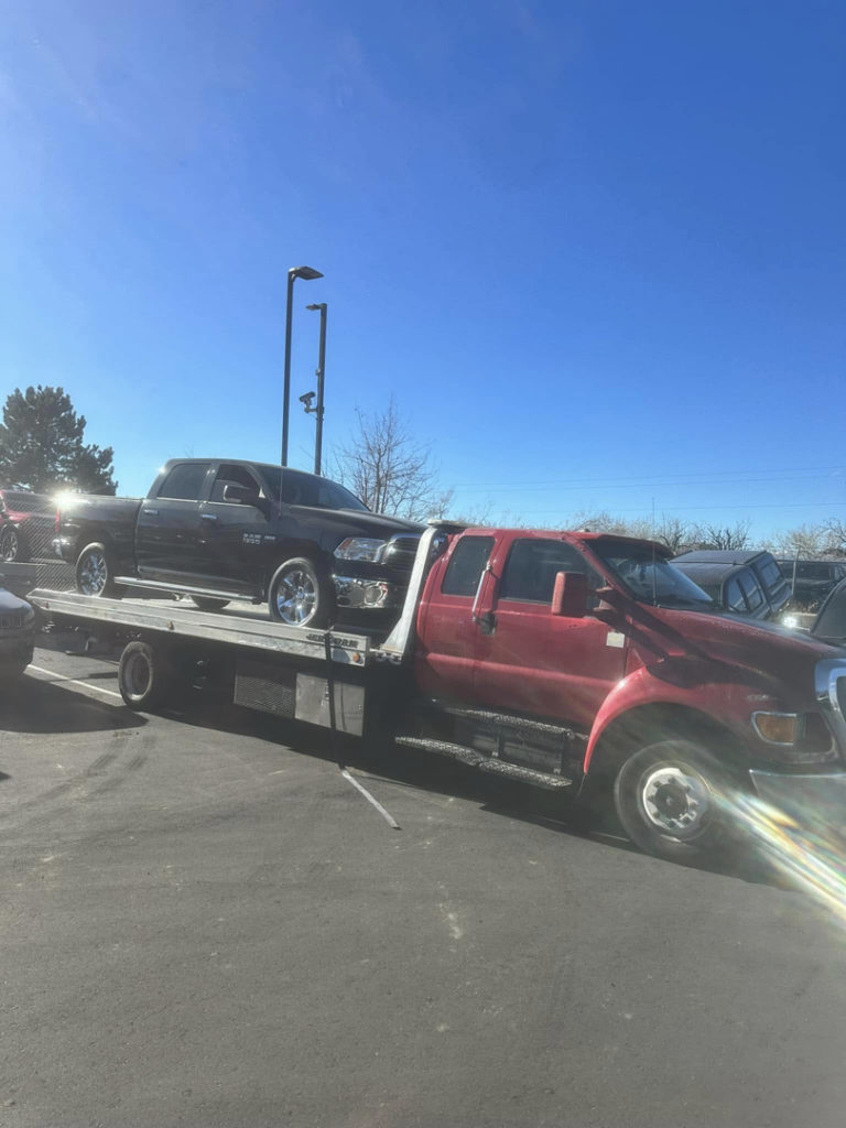 A black pickup truck being towed on a flatbed tow truck during the day by Luck's Unlimited Towing in Thornton, CO.