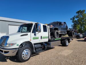A large black pickup truck being transported on a flatbed tow truck by Gem State Towing and Recovery in Caldwell, ID.