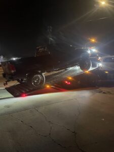 A black pickup truck being loaded onto a flatbed tow truck at night by Tiki's Towing LLC in Jacksonville, FL.