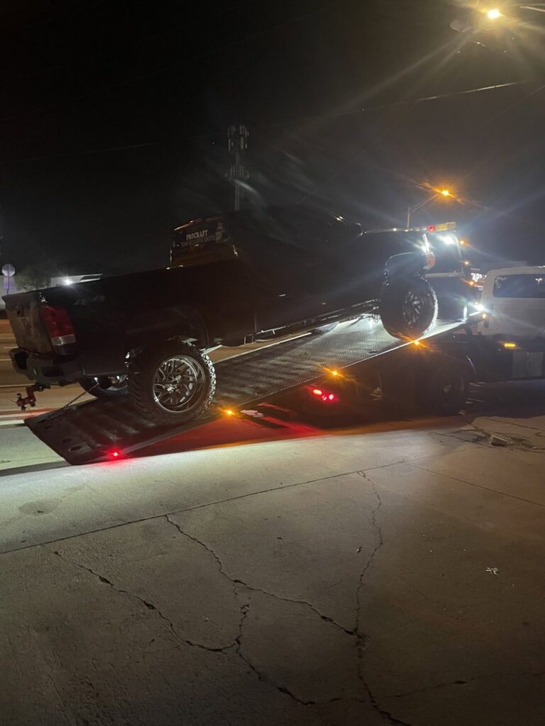 A black pickup truck being loaded onto a flatbed tow truck at night by Tiki's Towing LLC in Jacksonville, FL.