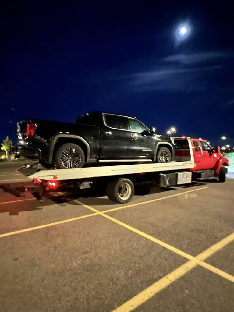 A black pickup truck being towed on a flatbed tow truck at night by Luck's Unlimited Towing in Thornton, CO.