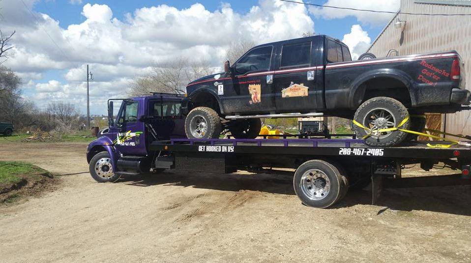 A black pickup truck being transported on a flatbed tow truck by Idaho State Towing and Recovery in Caldwell, ID.