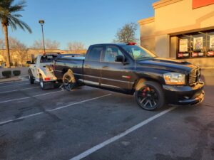 A black pickup truck with a missing wheel being towed by Caliber Towing in Phoenix, AZ.