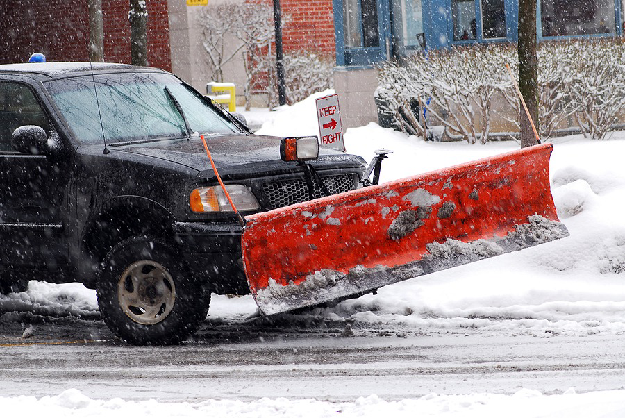 A black pickup truck equipped with a red snow plow on a snowy street, ready for snow removal by Green Works Lawn Care in Raleigh, NC.