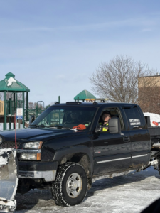 A black pickup truck with a snow plow and Eric's Winter & Landscape Services logo on the side, parked in a snowy area in Appleton, WI