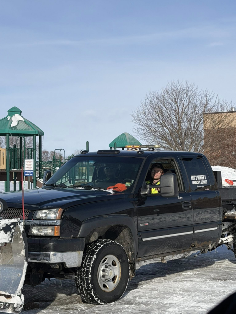 A black pickup truck with a snow plow and Eric's Winter & Landscape Services logo on the side, parked in a snowy area in Appleton, WI