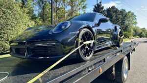 A black Porsche sports car securely strapped onto a TP Towing flatbed truck for transport in Tampa, FL.