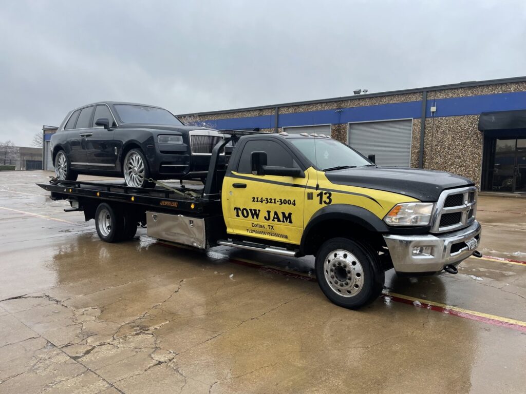 A black Rolls-Royce sedan being transported on a Tow Jam flatbed tow truck in Dallas, TX.