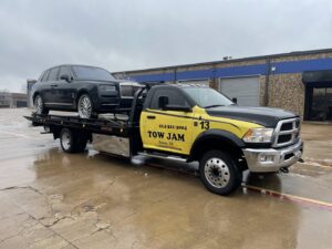 A black Rolls-Royce sedan being transported on a Tow Jam flatbed tow truck in Dallas, TX.
