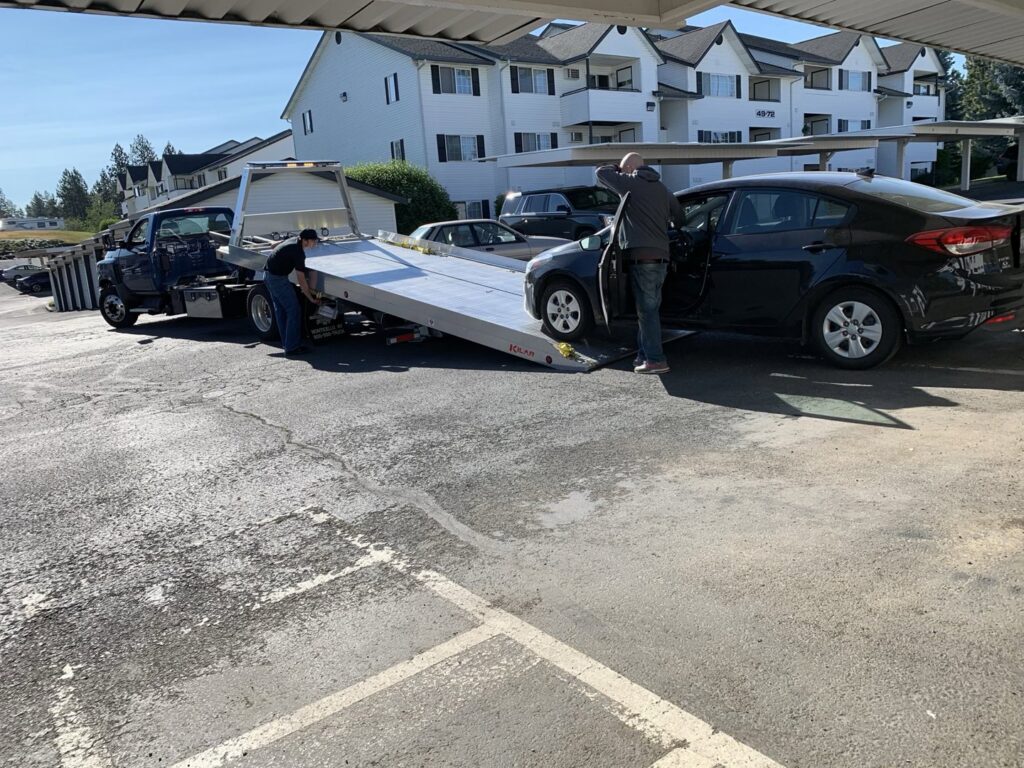 A black sedan being loaded onto a blue flatbed tow truck by Spokane Towing Services in Spokane, WA.
