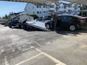 A black sedan being loaded onto a blue flatbed tow truck by Spokane Towing Services in Spokane, WA.