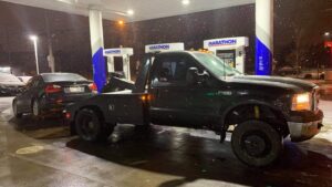 A black sedan being towed by a wrecker-style truck in snowy conditions by Quiñones Towing in Cleveland, OH.