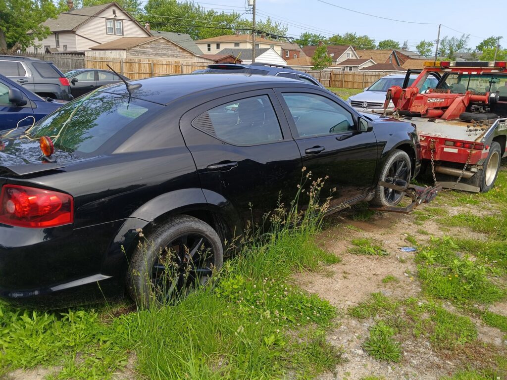 A black sedan being towed with its rear wheels on a wheel lift, demonstrating a towing service by Buffalo Towing Services in Buffalo, NY.