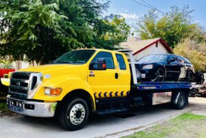 A black sedan secured on a yellow flatbed tow truck, ready for transport by A&A Towing Services in Bakersfield, CA.