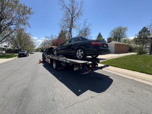 A black sedan being towed on a flatbed truck by Black Mamba Towing & Recovery Llc in Aurora, CO.