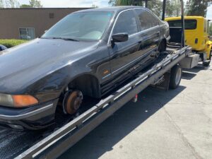 A black sedan without wheels being transported on a flatbed tow truck by All Roadside Towing San Diego, CA.