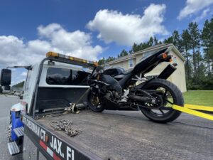 A black sportbike motorcycle being transported on a flatbed tow truck by Tiki's Towing LLC in Jacksonville, FL.