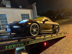 A black sports car being transported on a flatbed tow truck by ABOD Towing LLC in New Orleans, LA, at night.
