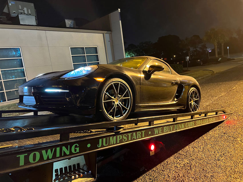 A black sports car being transported on a flatbed tow truck by ABOD Towing LLC in New Orleans, LA, at night.