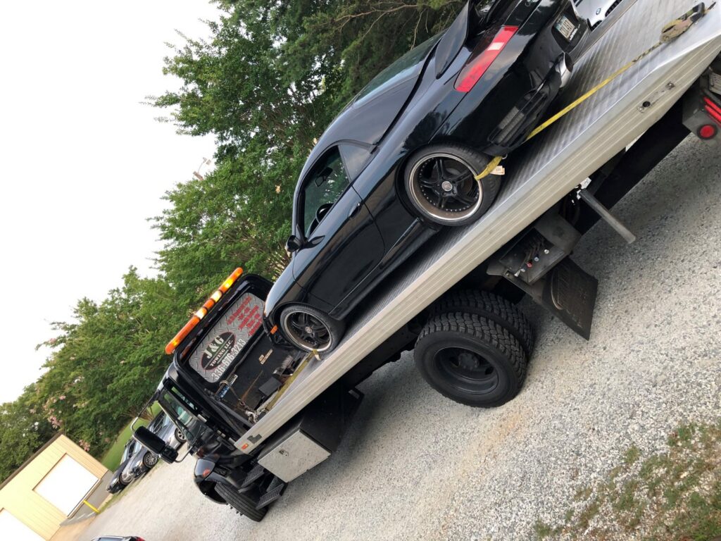 A black sports car securely loaded onto a flatbed tow truck from J & G Towing, LLC for transport in Greensboro, NC.