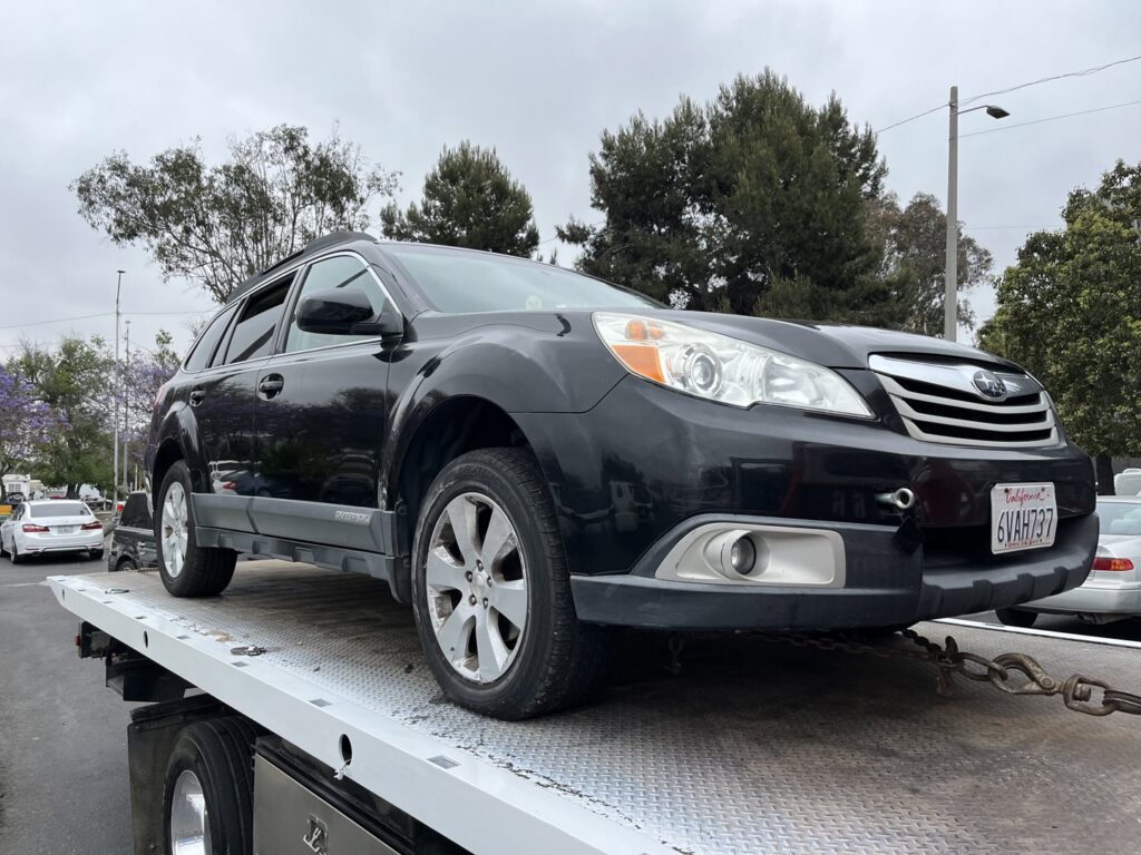 A black Subaru Outback being transported on a flatbed tow truck by All Roadside Towing San Diego, CA.