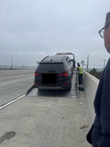 A black SUV being loaded onto a flatbed tow truck by Leos Towing Service on a bridge in Anaheim, CA.
