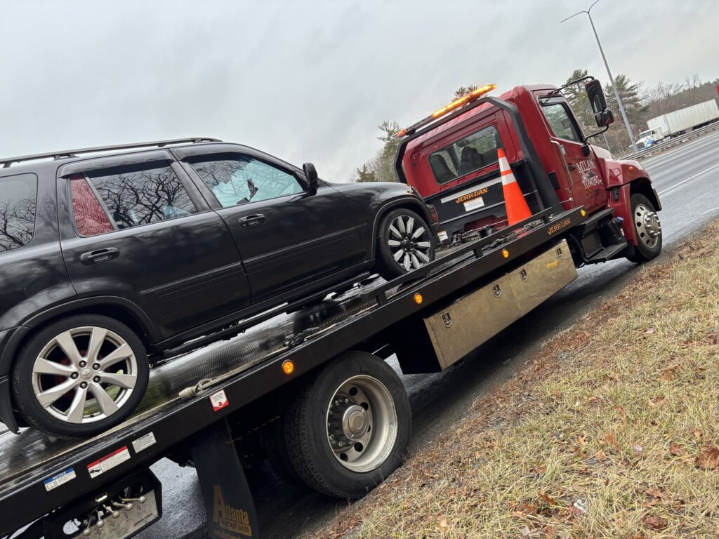 A black SUV being towed on a flatbed tow truck by Milan Towing inc. on the roadside in Milan, MI.