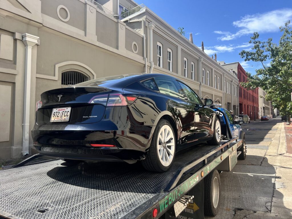 A black Tesla electric car being transported on a flatbed tow truck by ABOD Towing LLC in New Orleans, LA.