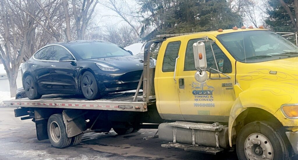 A black Tesla sedan loaded onto a Geely Towing flatbed tow truck in Fargo, ND.