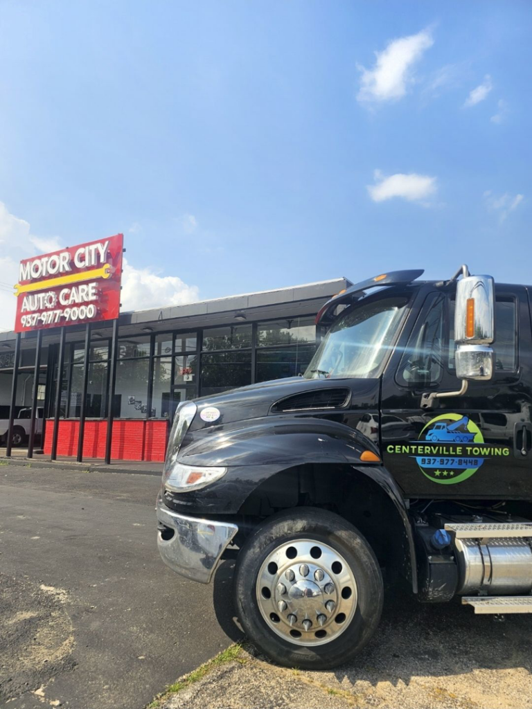 A black tow truck parked in front of Motor City Auto Care in Dayton, OH, ready to provide towing services.