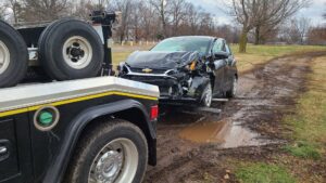 A black tow truck from Terry's Auto Service and Towing, LLC, recovering a damaged black car from mud in Springfield, MO.