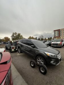 A black tow truck from Henderson Towing & Recovery LLC towing a black Tesla Model X in front of an apartment building in Denver, CO.