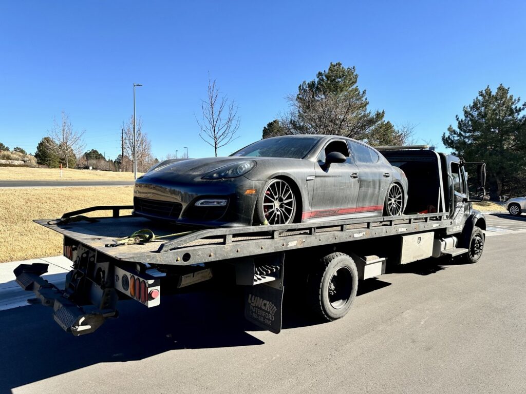 A black tow truck from Henderson Towing & Recovery LLC towing a Chevrolet Monte Carlo in a residential area of Denver, CO.