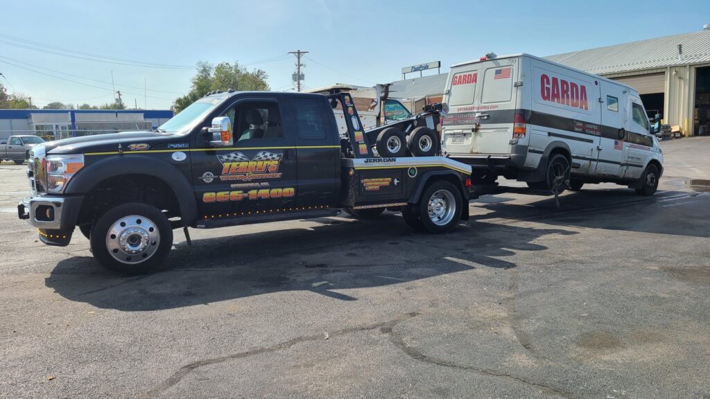 A black tow truck from Terry's Auto Service and Towing, LLC, towing a Garda armored van in Springfield, MO.